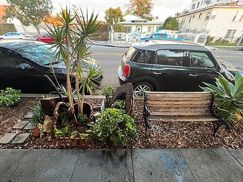 This is a photograph of the middle section of The Magical Park located on N Normandie Ave between Sunset Blvd and Hollywood Blvd in the East Hollywood district of Los Angeles. This particular picture captures a bench surrounded by different plants.