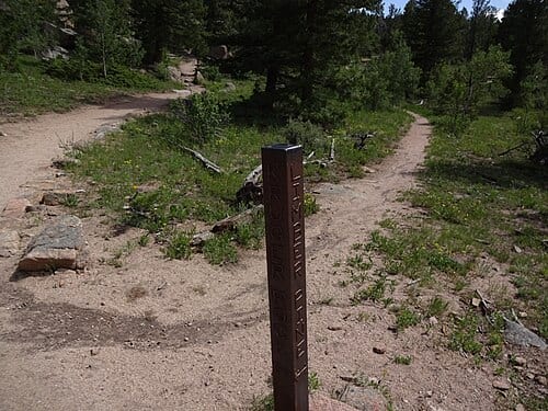 A vertical steel post sunk in the ground at the junction of the Limber Pine and Kruger Rock Trails in the Hermit Park Open Space, Larimer County, Colorado, US. The post has the names of the two trails written on it in weld bead on the appropriate sides.