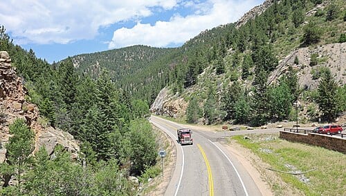 A view of Colorado State Highway 119 from the pedestrian bridge at Hidden Treasure Trailhead. The site is north of Black Hawk, Colorado . The view is generally towards the north. The creek partially visible on the left side of the highway is North Clear Creek.