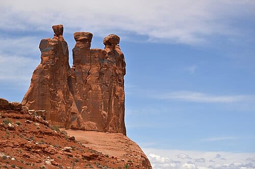 A rock formation called "The Three Gossips" stand watch at the edge of a cliff. Park Avenue, Courthouse Towers Section, Arches National Park, UT.