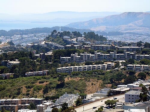 Probably taken from a rooftop near Mount Davidson . Homes on the eastern ridge of Mount Davidson are in the foreground. McLaren Park is in southeastern San Francisco. San Bruno mountains glow blue in the distance