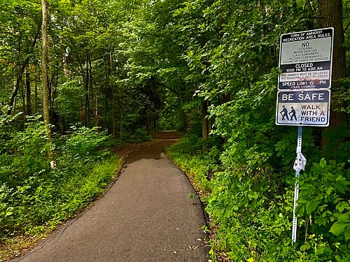 As seen in July 2022, a signpost at the head of a trail at Walton Woods Park in Amherst, New York advises visitors of the park's rules and regulations. 50 acres in area, Walton Woods is the verdant green space that serves as the nucleus of the Audubon New Community. One of three master-planned…